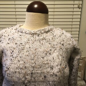 May include: A white sweater with a speckled pattern. The sweater has a round neckline and long sleeves.