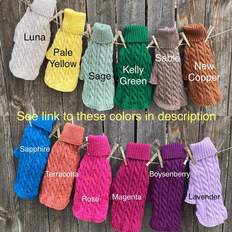 May include: A display of 12 different coloured knitted dog sweaters hanging on a wooden fence. The sweaters are all the same style, with a cable knit pattern and a turtleneck. The colours are: Luna, Pale Yellow, Sage, Kelly Green, Sable, New Copper, Sapphire, Terracotta, Rose, Magenta, Boysenberry, and Lavender.