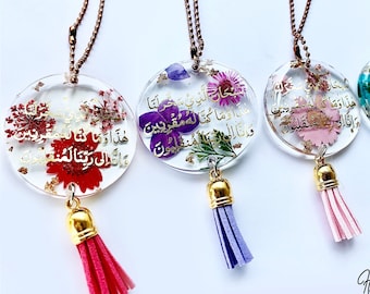 May include: Four round, clear resin ornaments with gold lettering and dried flowers. Each ornament has a gold chain and a tassel. The tassels are pink, purple, light blue, and teal.