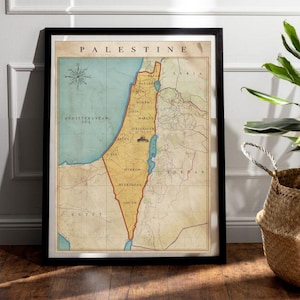 May include: Framed vintage map of Palestine with a black border. The map features a detailed illustration of the region, including the Mediterranean Sea and surrounding countries. The word "PALESTINE" is printed at the top. A potted plant in a woven basket sits to the right.