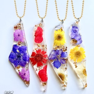 May include: Four resin pendants with gold-tone chain necklaces. Each pendant contains a pressed flower in shades of purple, red, and yellow, with gold leaf inclusions. The pendants have an irregular, geometric shape.