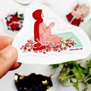 May include: A sticker featuring a woman in a red hijab praying on a green prayer rug with the Arabic words "Subhana Rabbiyal A'la" written in white. The sticker has a white background and a pink and green floral border.