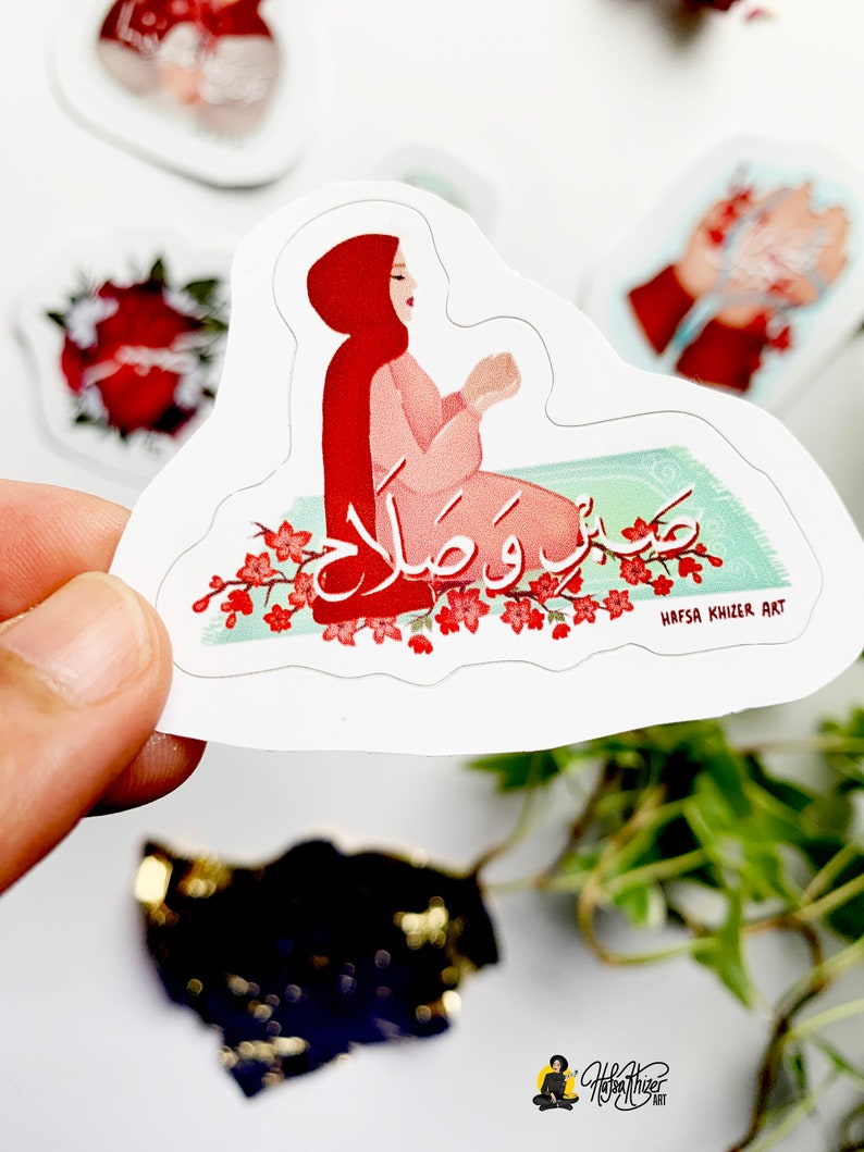 May include: A sticker featuring a woman in a red hijab praying on a green prayer rug with the Arabic words "Subhana Rabbiyal A'la" written in white. The sticker has a white background and a pink and green floral border.