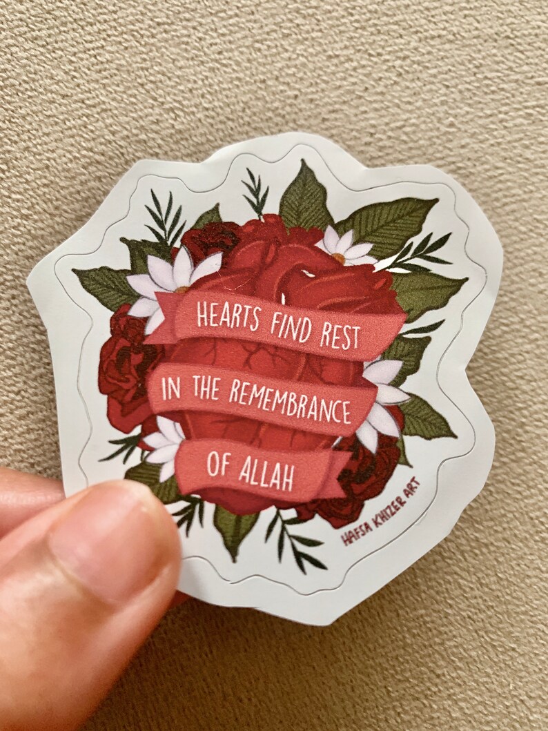 May include: A red heart surrounded by red and white flowers with green leaves. The heart has a red ribbon wrapped around it with the text "Hearts find rest in the remembrance of Allah". The sticker is designed by Hafsa Khizer Art.