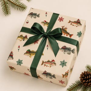 Op de afbeelding: Een rechthoekige geschenkdoos verpakt in crèmekleurig papier met een patroon van vissen met kerstmutsen, dobbers en rode en groene sneeuwvlokken. De doos is gestrikt met een donkergroen satijnen lint in een centrale strik.