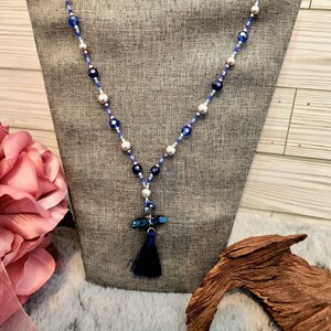 May include: A blue and silver beaded necklace with a blue tassel pendant. The necklace is displayed on a fabric-covered mannequin.