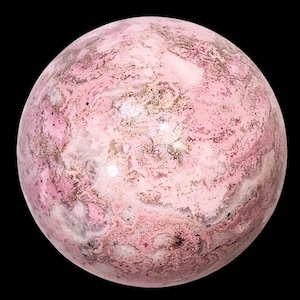 Puede incluir: Una esfera pulida con un patrón veteado rosa y beige. La piedra tiene un acabado brillante y parece ser un mineral natural. La esfera se encuentra sobre un fondo negro, resaltando sus colores y textura.