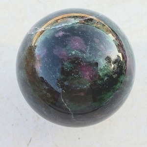 May include: A green and pink gemstone sphere with a gold rim. The sphere is polished and has a smooth surface.