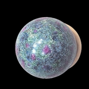 May include: A polished spherical stone featuring a mottled texture with a mix of deep magenta, dark blue, and forest green mineral inclusions throughout the surface, creating a variegated appearance with a smooth, reflective finish.