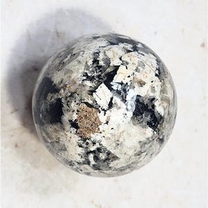 May include: A decorative sphere with a speckled pattern of black, white, and tan. The surface has a glossy finish, and the sphere appears to be made of a solid material. The overall effect is a unique, artistic design.