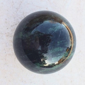 Könnte beinhalten: Eine glatte, polierte grüne und schwarze Kugel mit einem goldenen Rand. Die Kugel ist aus Naturstein und hat eine reflektierende Oberfläche.