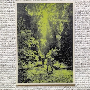 May include: A black and neon green print of a forest scene with three figures walking on a path. The image has a halftone dot pattern. The text "Mystic Multiples" is in the bottom right corner.