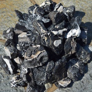 May include: A pile of black and white river rocks. The rocks are irregularly shaped and have a smooth, polished surface.