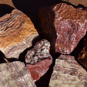 May include: Close-up of several pieces of banded red, white, and yellow striped stone. The stones have a rough, natural texture.