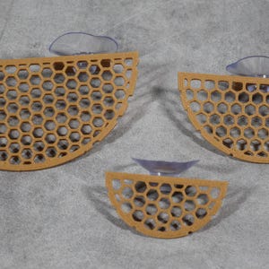 May include: Three brown, semi-circular, honeycomb-patterned suction cup shelves. The shelves are different sizes and are attached to a light-colored surface.