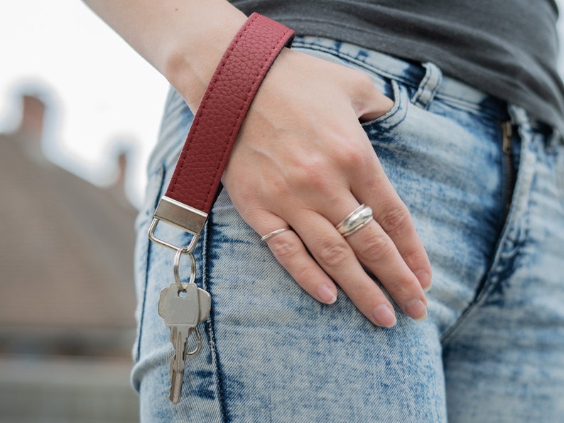 May include: A red leather key chain with a silver key ring and keys attached. The key chain is worn on a person's wrist.