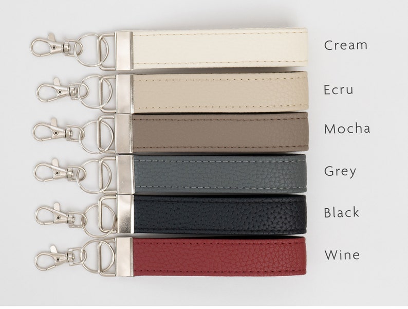 May include: Six leather keychains in different colors: cream, ecru, mocha, grey, black, and wine. Each keychain has a silver key ring.