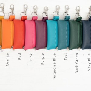 Puede incluir: Una colecci&oacute;n de nueve estuches rectangulares con cremallera y cierres de mosquet&oacute;n plateados, dispuestos en fila. Los estuches son de color amarillo, naranja, rojo, rosa, morado, azul turquesa, verde azulado, verde oscuro y azul marino, etiquetados.