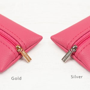 Puede incluir: Dos estuches rectangulares de color rosa brillante con superficies texturizadas y cremalleras rosas a juego. Un estuche tiene un tirador de cremallera de metal dorado, mientras que el otro tiene un tirador de metal plateado. El texto Gold y Silver aparece debajo.