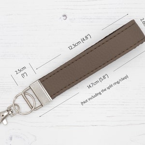May include: A brown leather keychain with a silver split ring and clasp. The keychain measures 5.8 inches long and 1 inch wide.