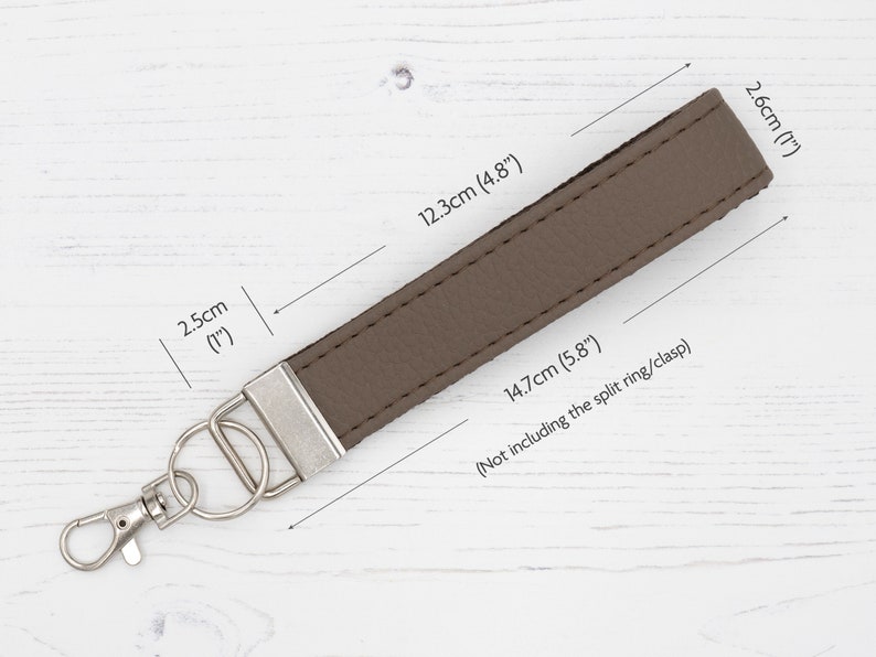 May include: A brown leather keychain with a silver split ring and clasp. The keychain measures 5.8 inches long and 1 inch wide.