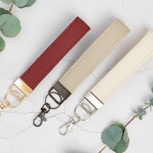 May include: Three leather keychains with metal key rings. The keychains are red, beige, and cream. The key rings are gold, black, and silver.