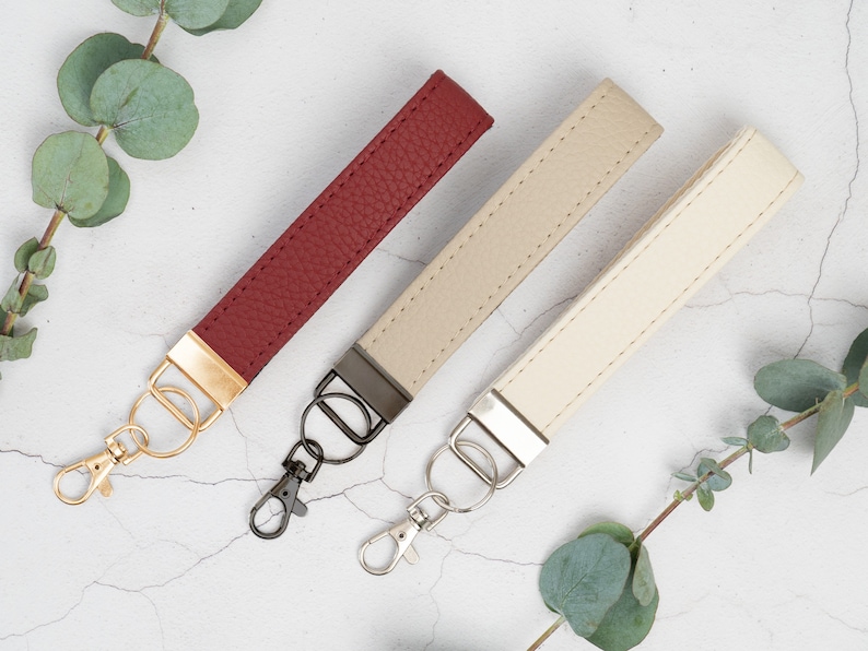 May include: Three leather keychains with metal key rings. The keychains are red, beige, and cream. The key rings are gold, black, and silver.