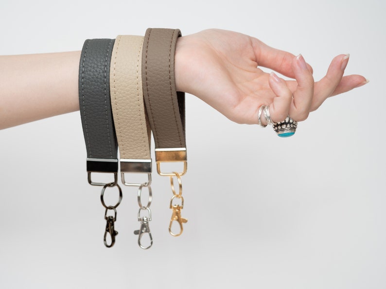 May include: Three leather keychains in gray, beige, and brown with gold and silver key rings.