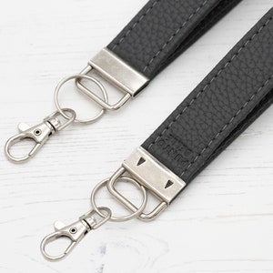 May include: A black leather camera strap with silver metal hardware and a silver key ring. The strap has the word "PUNTO" embossed on it.