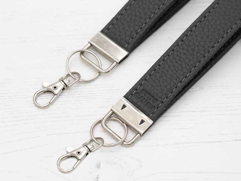 May include: A black leather camera strap with silver metal hardware and a silver key ring. The strap has the word "PUNTO" embossed on it.