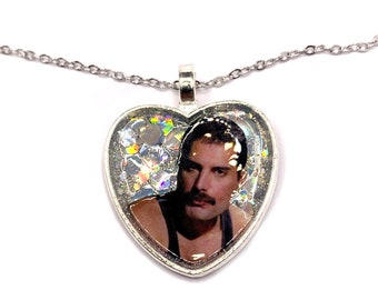 Könnte beinhalten: Eine silberfarbene Halskette mit herzförmigem Anhänger. Der Anhänger zeigt ein Porträt eines Mannes mit Schnurrbart, vor einem Hintergrund aus Glitzer. Die Kette ist filigran und der Anhänger ist etwa 4 cm breit.