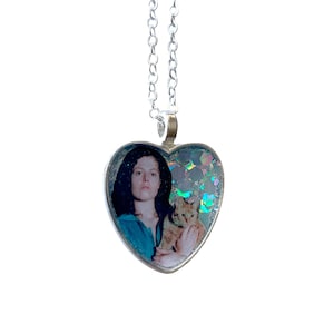 May include: A silver heart-shaped pendant necklace featuring a photo of a woman holding a cat. The photo is encased in iridescent glitter.