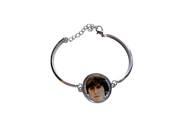 May include: Silver bracelet with a circular pendant displaying a portrait. The bracelet has a simple design with an adjustable chain. The pendant is framed with a glittery border.