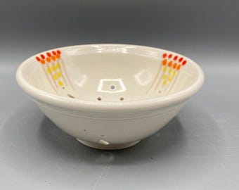 Op de afbeelding: Witte keramische zeef met een witte glazuur en oranje en gele geverfde stippen rond de rand.