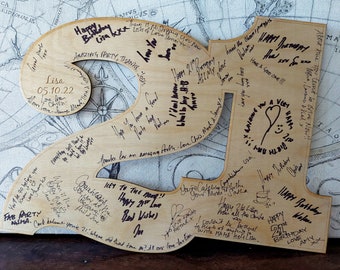 Op de afbeelding: Een houten 21e verjaardagsbord met een kompasontwerp en handgeschreven berichten. Het bord is versierd met een hart en een taart.