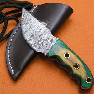 May include: A handcrafted knife with a Damascus steel blade and a green, brown and red wood handle. The handle has three brass accents. The knife is in a brown leather sheath.