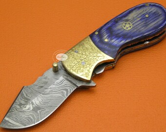 May include: A folding pocket knife with a blue and gold handle and a patterned steel blade. The handle has a floral design and a star-shaped emblem.