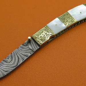 May include: A small, folding pocket knife with a patterned steel blade and a white mother-of-pearl handle with gold accents.