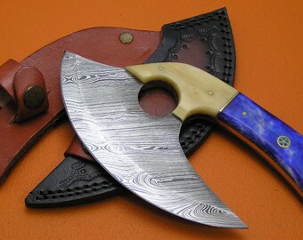 May include: A curved, Damascus steel knife with a blue and white bone handle. The knife has a ring in the handle and comes with a brown leather sheath.