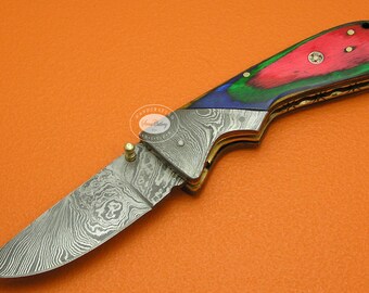 May include: A folding pocket knife with a Damascus steel blade and a colorful wood handle. The handle is red, green, and blue with a gold accent.