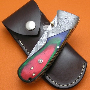 May include: A folding knife with a colorful wood handle and a damascus steel blade. The knife is in a brown leather sheath.