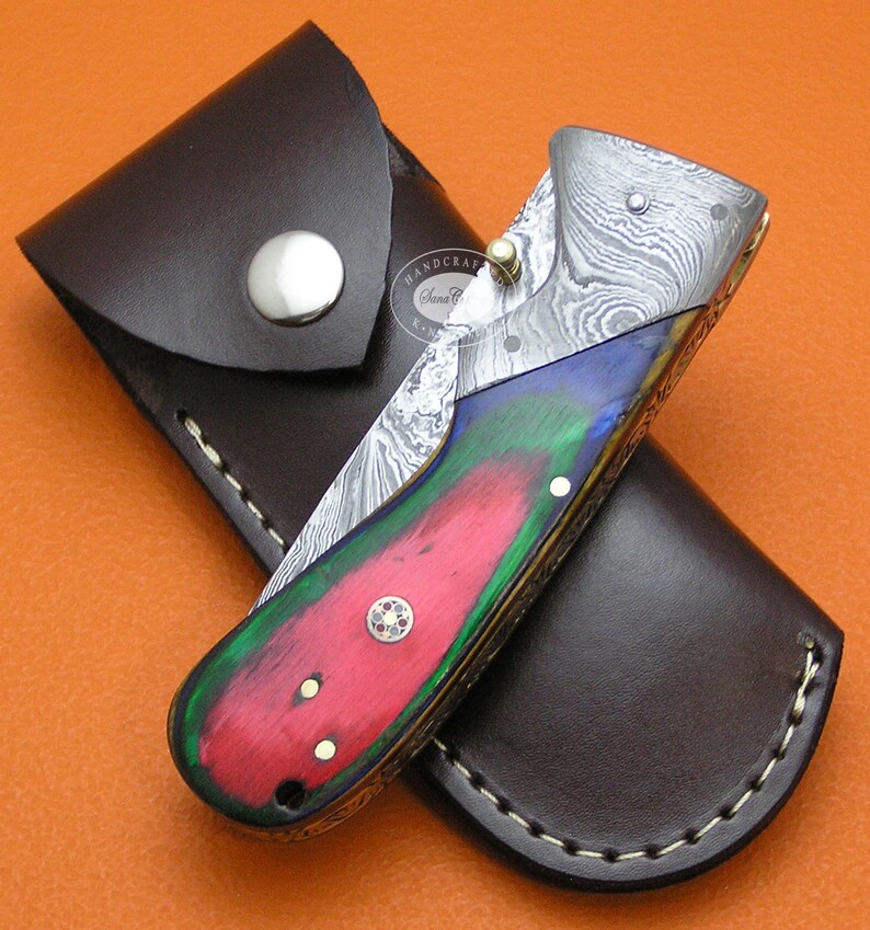 May include: A folding knife with a colorful wood handle and a damascus steel blade. The knife is in a brown leather sheath.
