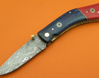 May include: A blue and red folding pocket knife with a patterned steel blade. The handle is made of wood with brass accents and decorative inlays.