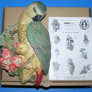 Könnte beinhalten: Eine Keramik-Wandskulptur mit zwei Papageien, die auf einem Ast mit rosa Blüten sitzen. Die Papageien sind grün und gelb mit realistischen Details. Die Skulptur ist Teil einer Sammlung von "Wild Life Wall Figures" von Bossons.