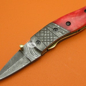 May include: A small, red and black pocket knife with a patterned blade and a red handle. The handle is made of bone and has a brass accent.
