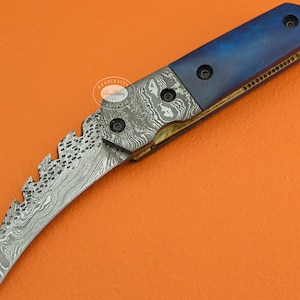 May include: A blue and silver folding knife with a curved blade and a serrated edge. The handle is made of blue wood and has a brass accent.