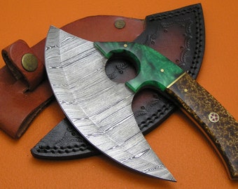 Op de afbeelding: Een gebogen mes van damaststaal met een groen-bruine handgreep. Het mes heeft een leren schede met decoratieve stiksels.