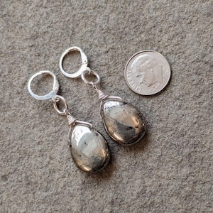 May include: A pair of silver earrings with teardrop-shaped pyrite stones. The earrings have lever-back closures and are next to a U.S. dime for size comparison. The pyrite stones have a metallic, reflective appearance.