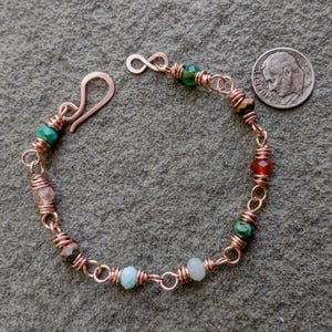 May include: A handmade copper bracelet with colorful gemstone beads. The bracelet features a hook clasp and an infinity-shaped end. The beads are various colors, including green, red, and pink. A U.S. dime is next to the bracelet for size comparison.