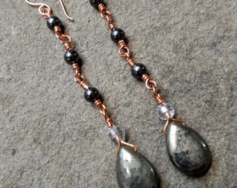 May include: A pair of long, dangling earrings with a copper wire chain and black beads. The earrings are topped with a teardrop-shaped, dark gray stone.